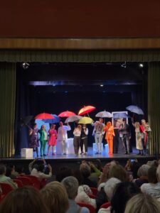 Foto de la compañía sobre el escenario portando paraguas